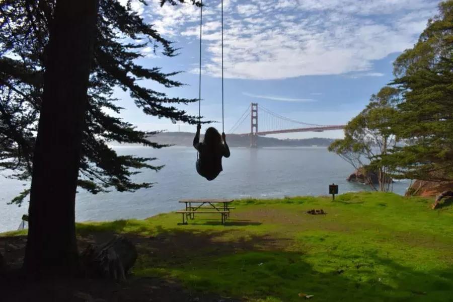 Una mujer se balancea en un columpio de un árbol con vistas al puente Golden Gate. 加州贝博体彩app.